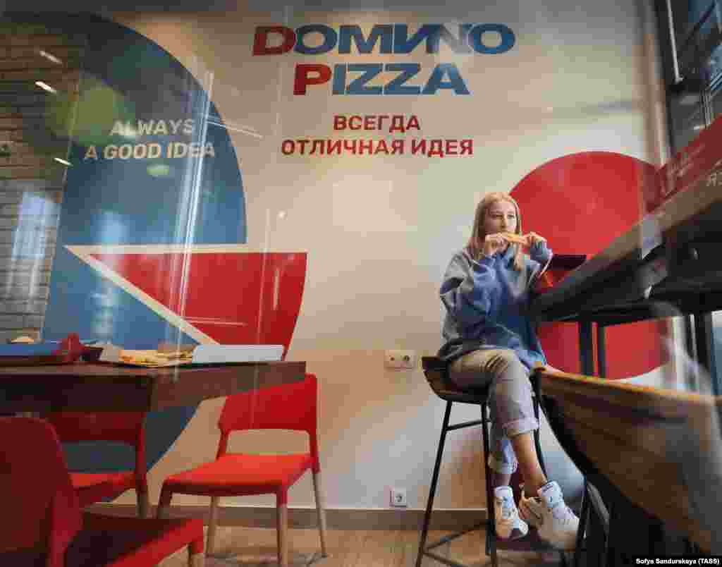 A woman enjoys a slice in a rebranded Domino's Pizza outlet in Moscow that was reopened on August 30 as "Domиno Pizza," with the Latin "i" in the name replaced with the equivalent Cyrillic letter "и."