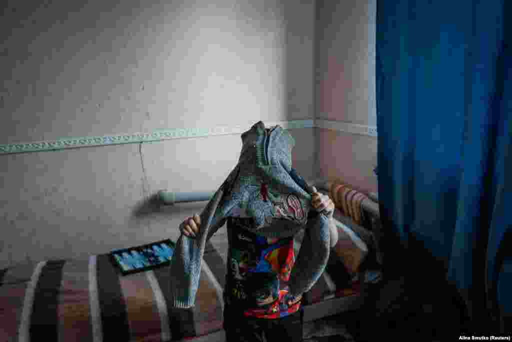 Руслан, 9-річний переселенець із Торецька, одягається тепліше у притулку, де він зараз проживає. Сім'ї з дітьми зазвичай залишаються в притулку для внутрішньо переміщених осіб на кілька днів, тоді як літні евакуйовані, яким важче знайти постійне житло, іноді перебувають там місяцями