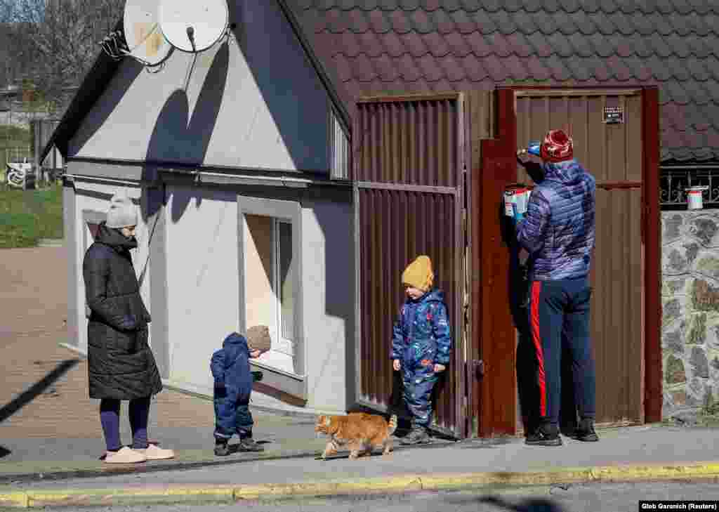 Дарія (ліворуч) дивиться, як її чоловік Максим фарбує ворота перед їхнім відремонтованим будинком. Поруч граються їхні діти. Буча, 30 березня 2023 року Рік тому на вулиці перед їхнім будинком теж лежали тіла убитих російськими військовими людей. 