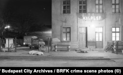 Fotografija iste željezničke stanice kao na prethodne dvije fotografije na kojoj se vidi tijelo koje leži pod plahtom