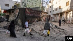 Ljudi nose kese sa humanitarnom pomoći dok hodaju među ruševinama nakon vojne operacije u izbjegličkom kampu Dženin na okupiranoj Zapadnoj obali, 5. juli
