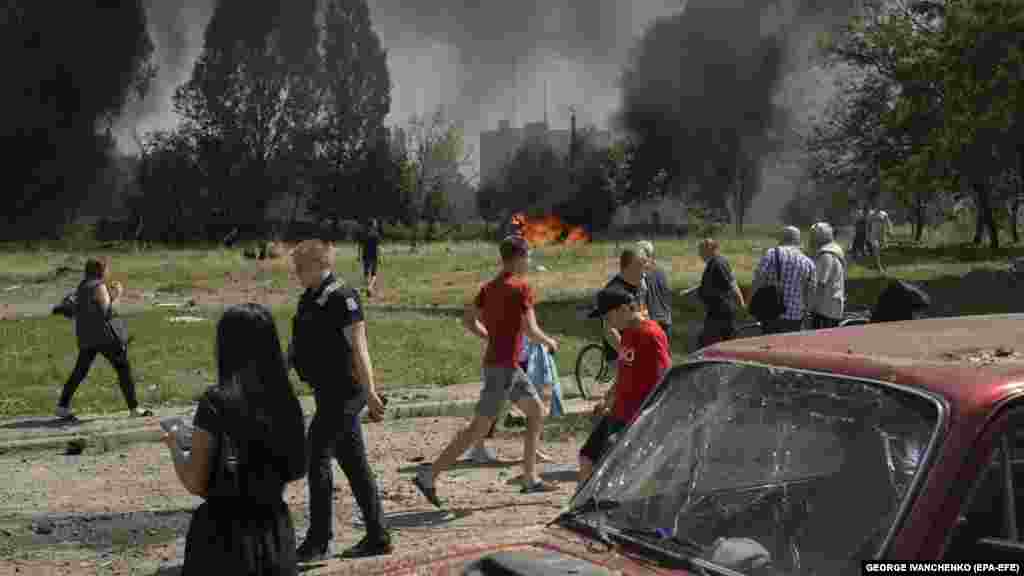 Ljudi na mjestu napada dok automobili gore u blizini.