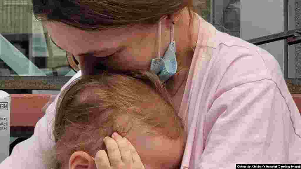 Žena tješi dijete ispred bolnice Ohmadit nakon napada 8. jula. Kremlj je tvrdio da je za eksploziju u krugu bolnice kriva zalutala ukrajinska protivvazdušna raketa, ali snimljene slike projektila pokazuju prepoznatljivu siluetu krstareće rakete Kh-101, oružja koje koristi isključivo ruska vojska. Ukrajinske vlasti tvrde da je projektil pogodio "tačan cilj za koji je bio programiran" usred talasa ruskih napada širom Ukrajine tog dana.