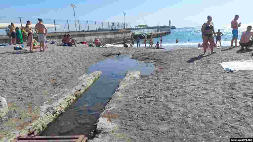 А вот и причина, почему местные жители не купаются на этом участке пляжа. Канализационные стоки продолжительное время стекают здесь в море. Со временем образовалось русло «реки», однако зловонное течение не мешает туристам «отдыхать» здесь с детьми