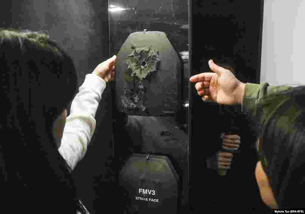 Відвідувачі виставки оглядають кульові пошкодження на бронепластині. На сайті виставки є пояснення стосовно використання «броньованих плит, які вже врятували чиєсь життя на полі бою, а зараз отримали другий шанс, щоб врятувати життя людини за допомогою таланту відомих художників»