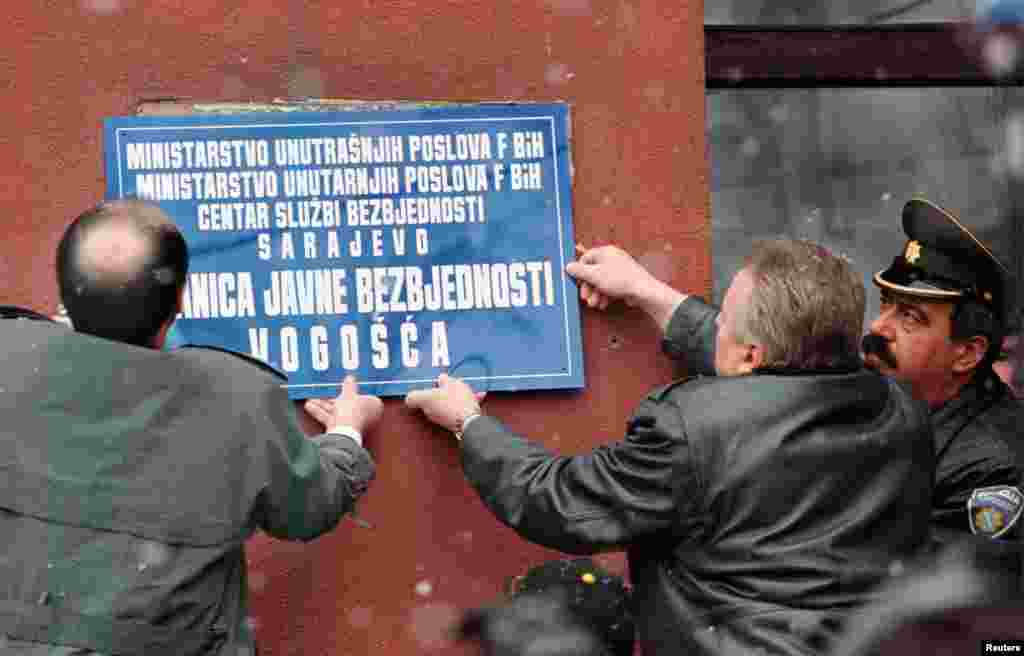Policija Federacije BiH, na čelu sa ministrom unutrašnjih poslova Avdom Hebibom (C), postavlja novi znak na zidu policijske stanice u Vogošći, sarajevskog naselja koje su tokom opsade grada pod kontrolom držale snage bosanskih Srba i koje je Dejtonskim sporazumom pripalo Federaciji BiH. 23. februar 1996. 