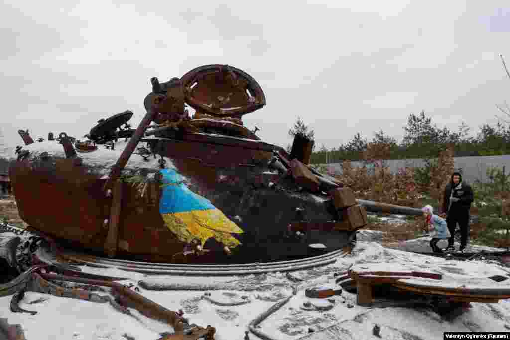 Люди стоять біля знищеного російського танка, на якому відомий вуличний художник Tvboy намалював ще одного голуба миру в кольорах українського прапора. Дмитрівка, Київщина, 29 січня 2023 року