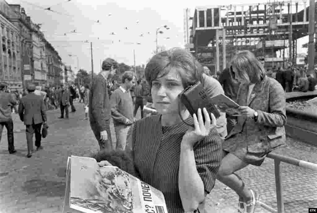 Женщина слушает последние новости. Радио во время вторжения играло важную роль. Чехословацкое радио передавало новости до того момента, пока помещение не заняли войска. Это произошло после серьезного столкновения у здания радио, где 17 молодых людей повредили танковые баки с бензином и подожгли его. Они надеялись, что это поможет задержать военных.  