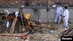 Dva člana porodice stoje pored lomače koja odnosi tjelo njihovog rođaka preiminulog od posledica infekcije korona virusom u glavnom gradu Indije Nju Delhiju. 22. spril 2021. 