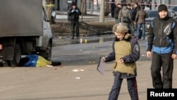 A policewoman walks near the body of a victim covered by a Ukrainian national flag at the site of a bomb attack in Kharkiv on February 22 which killed three people.