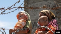 Ethnic Uzbek refugees walk behind a barbed wire fence as they queue to return to Kyrgyzstan at the border crossing near the city of Osh