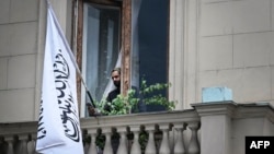 ავღანელი მოხელე მობილური ტელეფონით ავღანეთის ისლამური საამიროების დროშასთან, მოსკოვში, ავღანეთის საელჩოს აივანზე. 4 ივლისი, 2025 წელი