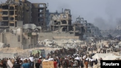 Граждани на град Газа на фона на разрушени от израелски удари сгради.