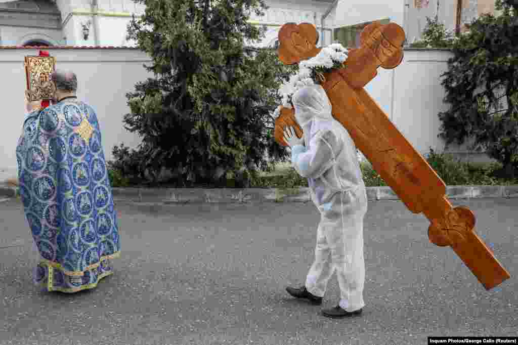 Volonter u zaštitnoj opremi nosi krst tokom religijske službe u Bukureštu na Veliki petak, 17. aprila 2020. godine.