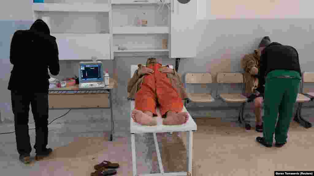 Strani zatvorenik leži na krevetu pored liječnika u zatvoru u gradu Hasaka, 7. siječnja 2020. Uvjeti u zatvoru u blizini Hasake, koji je najprije bio škola, bili su znatno lošiji od onih u središnjem zatvoru. U prizemlju bolnice oko 100 muškaraca leži na krevetima kojih nema dovoljno za sve bolesne i ozlijeđene zatvornike te pritvorenike. Nekoliko ih je bilo u narančastim kombinezonima, slično onima koje su zarobljenici "Islamske države" često nosili pred pogubljenja.