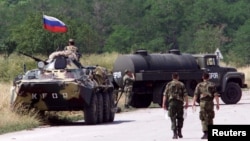 Vojnici Jugoslavije prolaze pored vozila ruske vojske na aerodromu Slatina u blizini Prištine 12. juna 1999. Oko 200 ruskih vojnika zaustavljeno je tada oko 100 metara od prištinskog aerodroma na Kosovu nakon što su preko noći prešli iz Srbije na Kosovo uoči dolaska mirovnih snaga predvođenih NATO-om.