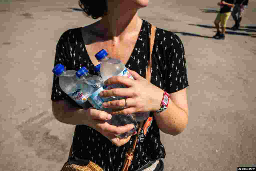 Një pjesëmarrëse e një festivali muzikor në jug të Francës duke bartur shishe me ujë të frohtë, më 29 qershor.