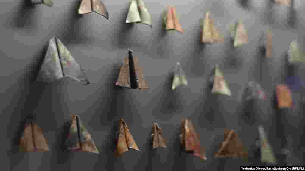 Фло Касеару, «Бунт». Зменшені залізні копії паперових літачків під склом – частина більшої інсталяції, у центрі якої – відео, що зображує ремонтні роботи в будинку, де живе художниця. Будівельники знімали залізні пластини з даху й згортали подібно до паперових літачків. Для Касеару ця фігура стала символом мілітаризації сучасних взаємин між країнами, зокрема, між Заходом і Росією.