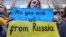 Žena na protestu u Briselu ispred nemačke ambasade drži transparent tokom demonstracija podrške Ukrajini, 11. mart 2022.