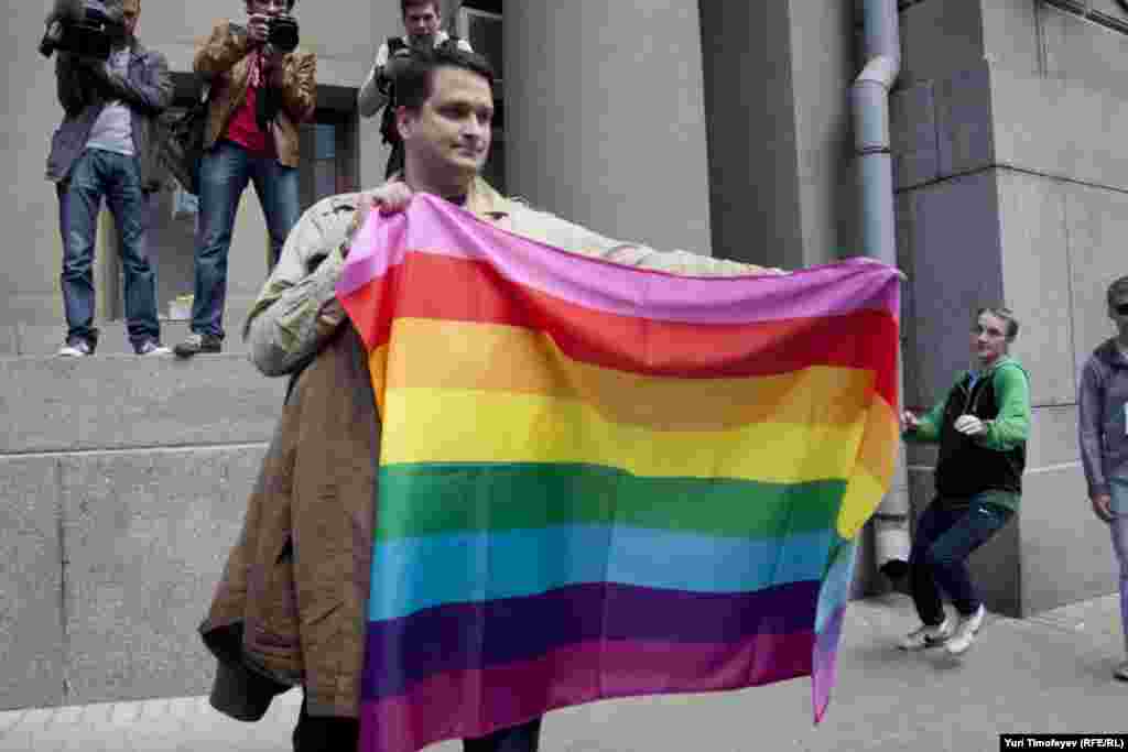 Гей-активист разворачивает радужный флаг, сзаду уже набегает "противник" гей-парадов. 