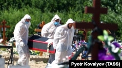 Gravediggers wearing personal protective equipment bury a person who died from COVID-19, in a cemetery on the outskirts of St. Petersburg.