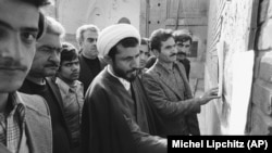 მოლა მოქალაქეებთან ერთად კითხულობს გადასახლებული ისლამური ლიდერის, აიათოლა რუჰოლა ხომეინის ბოლო სიტყვებს თეირანის ბაზარში. 1978 წლის 16 დეკემბერი.