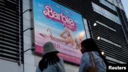 Жінки перед рекламним плакатом фільму «Барбі» в Токіо
