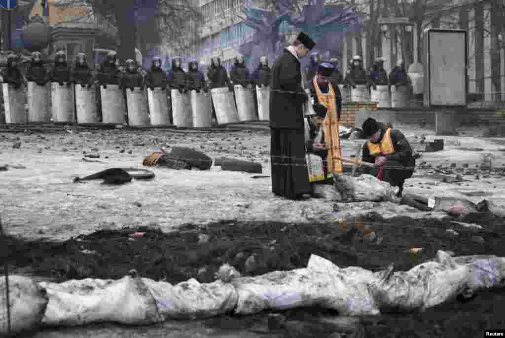 Священики запалюють свічки під час служби на місці недавніх зіткнень біля барикад на Грушевського, Київ, 13 лютого 2014 року