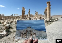 Fotograf drži svoju fotografiju Arc du Triomphe u Palmiri snimljenu 14. marta 2014. ispred ostataka povijesnog spomenika nakon što su ga militanti "Islamske države" uništili u oktobru 2015.