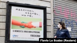 Žena prolazi pored plakata u Milanu sa rukama u bojama kineske i italijanske zastave na kojem piše "Neprijatelj je virus, ne narod. Napred, Kina" 10. marta 2020. godine