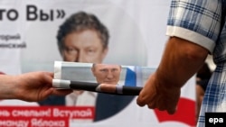 Сторонник "Единой России" раздает газеты с портретом президента Путина у предвыборного плаката партии "Яблоко"