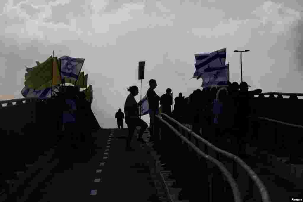 Demonstranti stoje na mostu dok, zajedno s drugima, blokiraju glavnu cestu tokom demonstracija zahtijevajući trenutni kraj rata i oslobađanje svih talaca koji su oteti tokom smrtonosnog napada Hamasa na Izrael 7. oktobra 2023. godine, u Jakumu blizu Tel Aviva, 26. avgusta 2025.