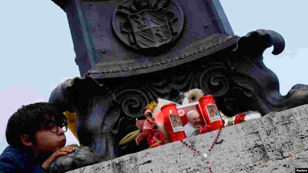 Leo, 9 godina, pokušava da ugasi svijeće postavljene pored fotografije pape Franje, dok ljudi učestvuju u molitvama nakon smrti pape, na Trgu Svetog Petra, u Vatikanu.