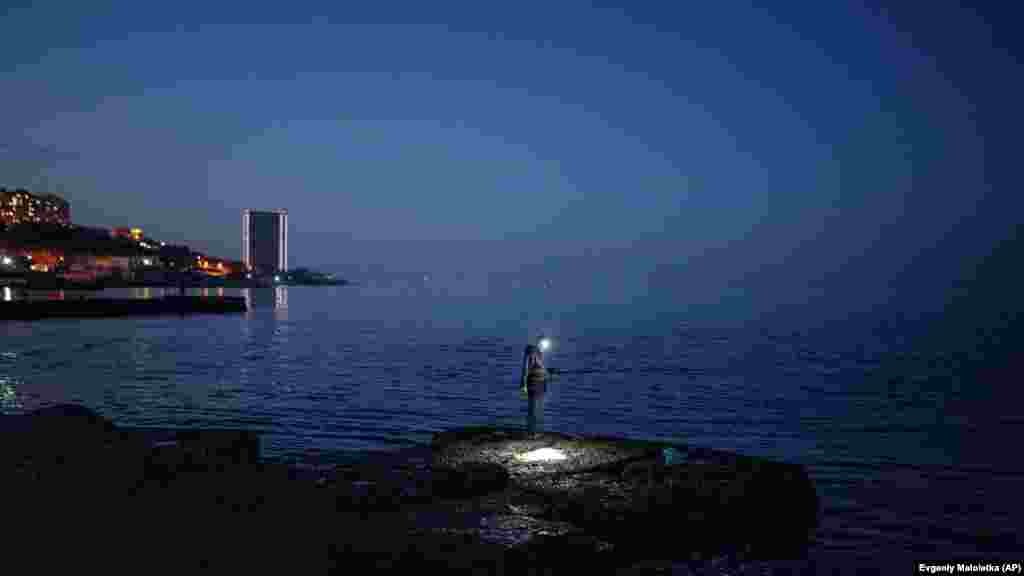 Čovjek peca na lukobranu na plaži Arkadija u ukrajinskom lučkom gradu Odesi.