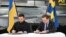 Prim-ministrul suedez Ulf Kristersson (R) și președintele ucrainean Volodimir Zelenski semnează o scrisoare de intenție pentru dezvoltarea capabilităților aeriene la Linköping, Suedia, pe 22 octombrie 2025.