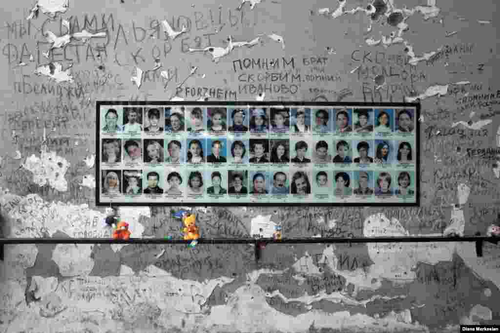 At School No. 1, portraits of more than 300 victims hang in the gymnasium where 1,100 children, parents, and teachers were held hostage for 52 hours. The school stands in ruins, and the room itself has been largely untouched since 2004. Bullet holes and haunting inscriptions of "we remember" adorn the walls; there is a charred gym ladder to one side and blackened basketball hoops at either end. An Orthodox cross has been placed in the middle of the gym floor, surrounded by freshly opened bottles of water left to commemorate the captives, who endured over two days in fierce summer heat with almost no water. Residents continue to bring teddy bears, model cars, and other toys in memory of the 186 children who were killed here.  