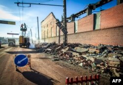 Робітники ремонтують лінію електропередач біля стіни місцевого цинкового заводу, який був пошкоджений в результаті ударної хвилі від вибуху метеорита.