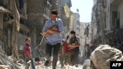 Na ovoj fotografiji od 11. septembra 2016. godine, sirijski muškarci koji nose bebe probijaju se kroz ruševine uništenih zgrada nakon prijavljenog vazdušnog udara na pobunjeničko naselje Salihin u Alepu, gradu na sjeveru Sirije. 