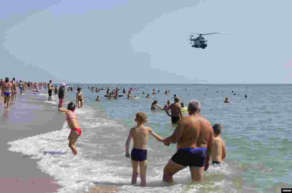 Люди спостерігають за вертольотом ВМС України, який пролітає над пляжем біля смт Сергіївка (Одеська область), 6 серпня 2019 року