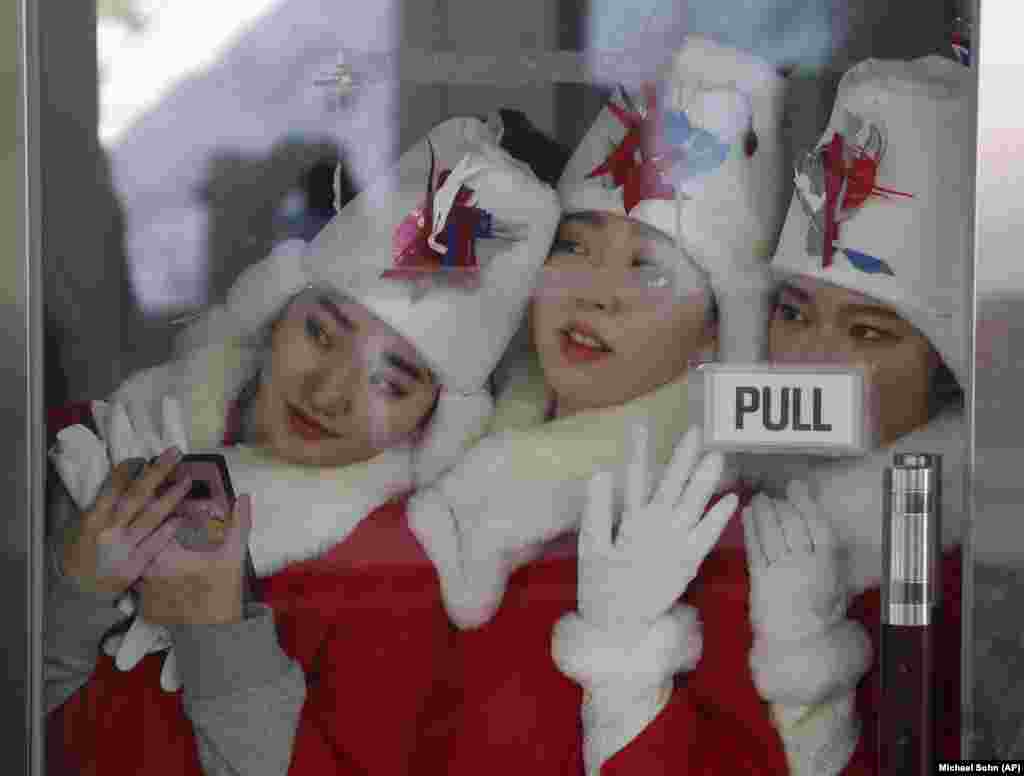 Дівчата, які роздають нагороди на церемонії переможців, спостерігають за спортсменами під час фіналу з чоловічого скелетону 