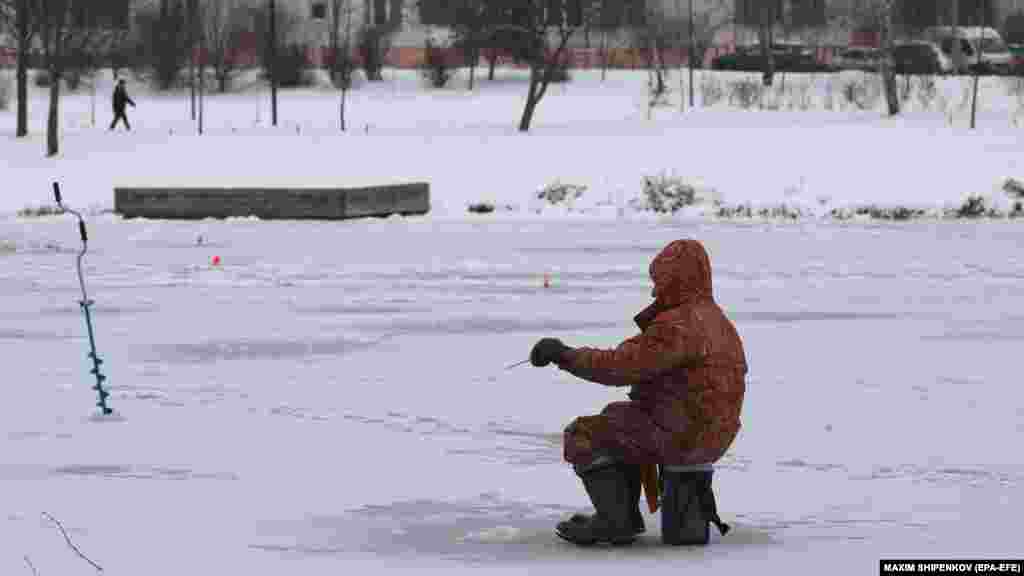 Muškarac lovi ribu u zaleđenom jezercu u stambenoj četvrti u Moskvi. 
