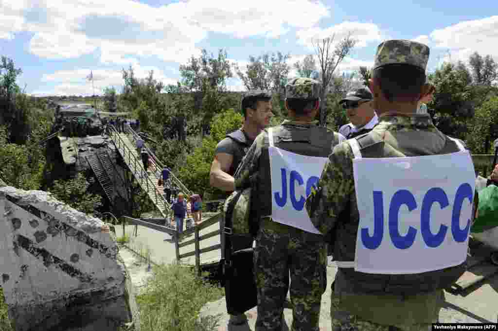Українські офіцери Об’єднаного центру контролю та координації і співробітники ОБСЄ спостерігають за тим, як люди проходять через зруйнований міст між підконтрольною Києву територією і територією, яку контролюють гібридні російські збройні формування. Станиця Луганська, 1 серпня 2019 року