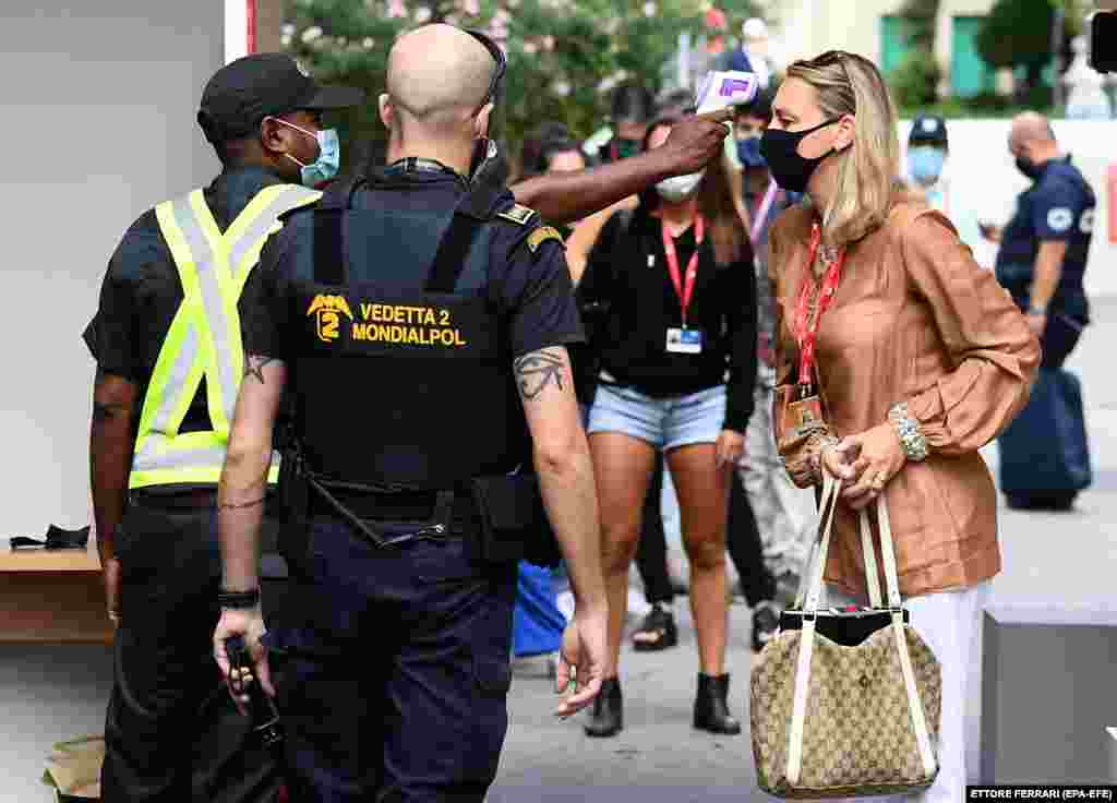 Zaštitar nosi masku za lice i provjerava tjelesnu temperaturu ženi na ulazu u prostor za održavanje 77. Venecijanskog filmskog festivala, 2. septembar, 2020.