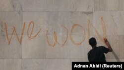 Mladi demonstrant na zidu parlamenta ispisuje poruku "Pobedili smo!"