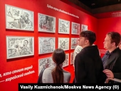 მნახველები ათვალიერებენ პროპაგანდისტულ ნახატებს, სადაც ასახულია ჩრდილოეთ კორეის ჯარისკაცების ბრძოლა უკრაინელების წინააღმდეგ