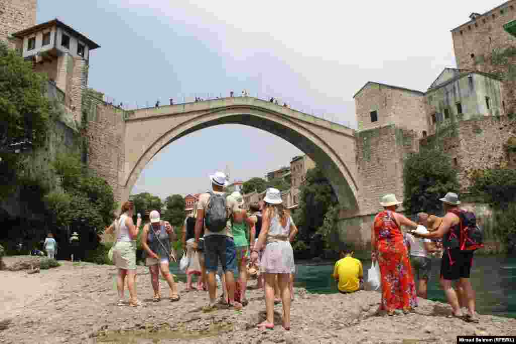 Grupa turista sa šeširima na glavama ispod Starog mosta u Mostaru.