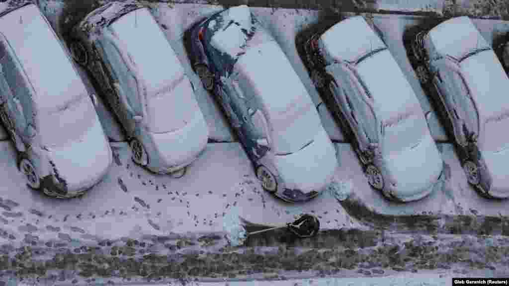 Radnik čisti ulicu u kojoj su automobili prekriveni prvim ovosezonskim snijegom u Kijevu 21. novembra.