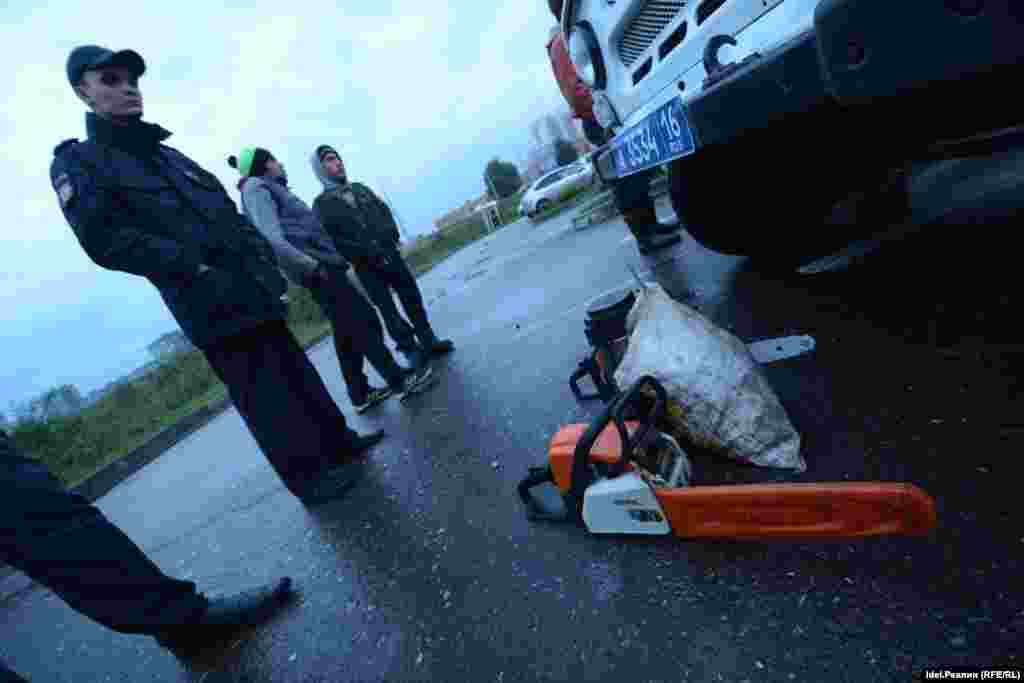 Гастарбайтеры разоружаются перед "УАЗиком", складывая на асфальт у капота бензопилы и сумки